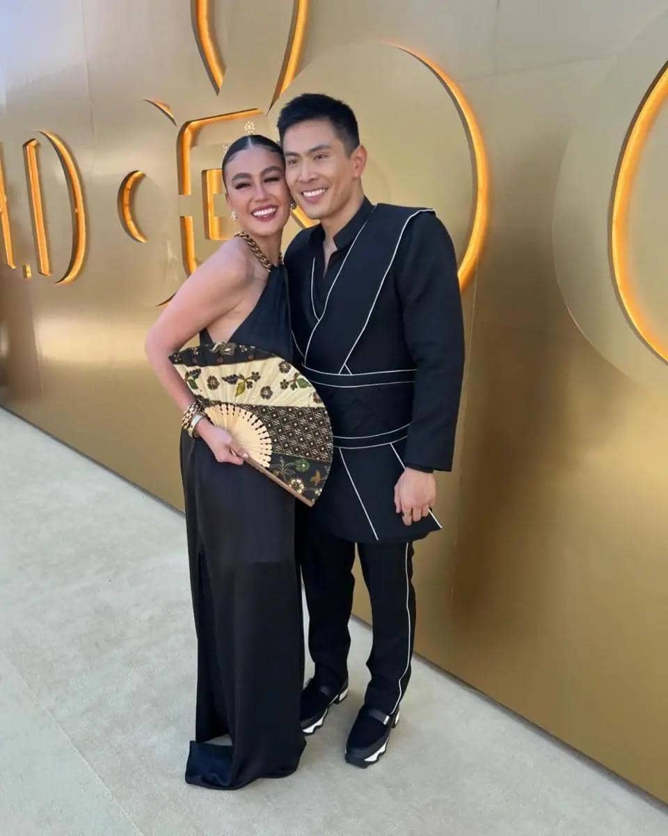 Seorang perempuan dan laki-laki berpose bersama di karpet acara Gold Gala 2024 dengan latar dinding emas berlogo besar.