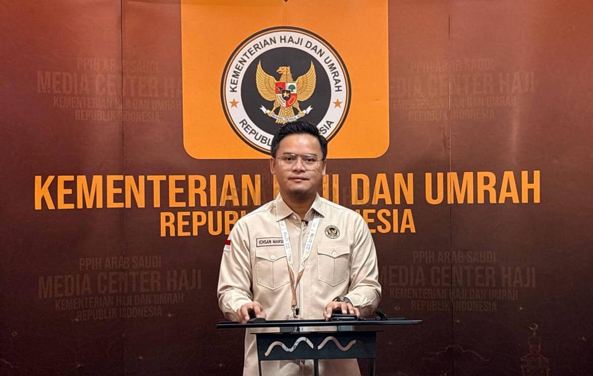 Seorang pria berdiri di podium dengan latar belakang logo dan tulisan Kementerian Haji dan Umrah Republik Indonesia.