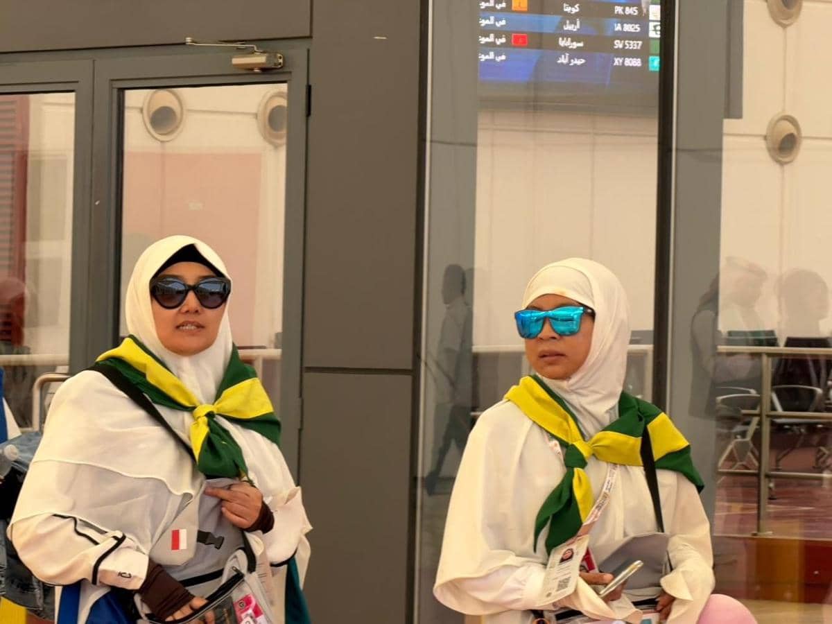 Dua jemaah haji Indonesia mengenakan pakaian ihram dan syal hijau kuning tiba di Bandara Internasional King Abdulaziz, Jeddah.