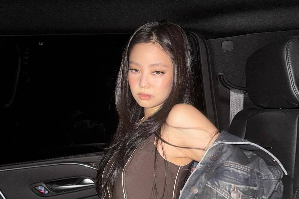 Seorang perempuan berambut panjang mengenakan atasan tanpa lengan berwarna gelap dan jaket denim, duduk di dalam mobil pada malam hari.