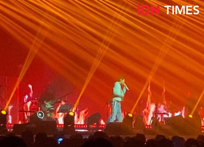 Penyanyi tampil di atas panggung konser WOODZ di The Kasablanka, Jakarta, dengan pencahayaan oranye dan efek visual api yang dramatis.