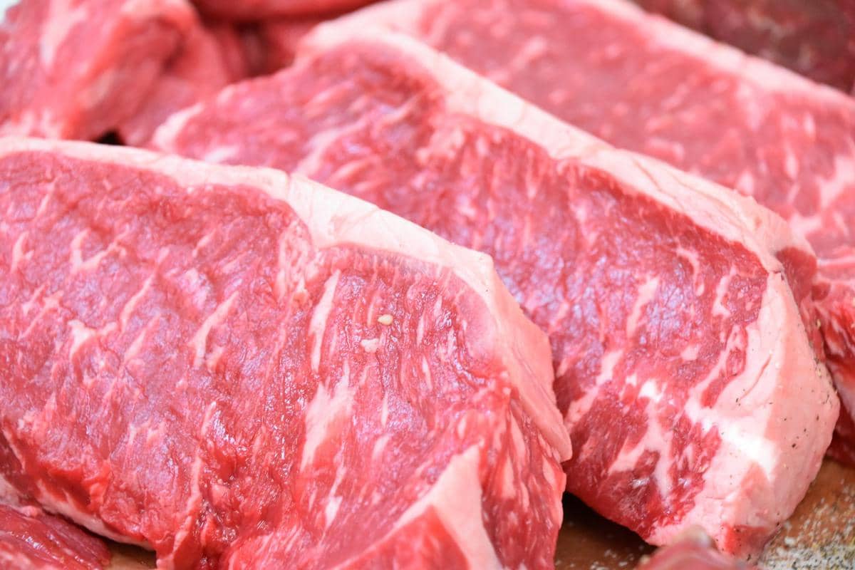 Potongan daging sapi merah segar dengan serat lemak putih yang terlihat jelas di atas permukaan meja pemotongan.