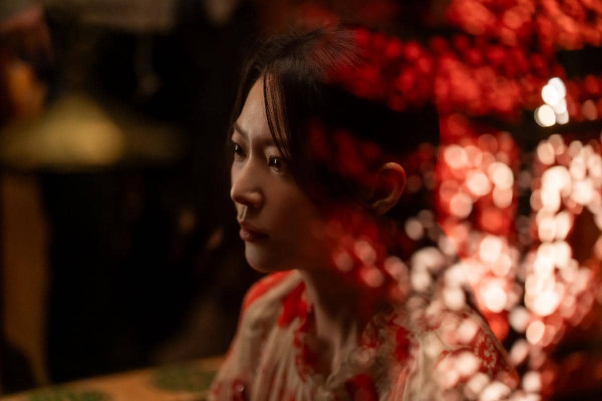 Seorang perempuan menatap ke samping dalam pencahayaan redup dengan pantulan cahaya merah di sekitarnya, diambil dari drama Perfect Crown.
