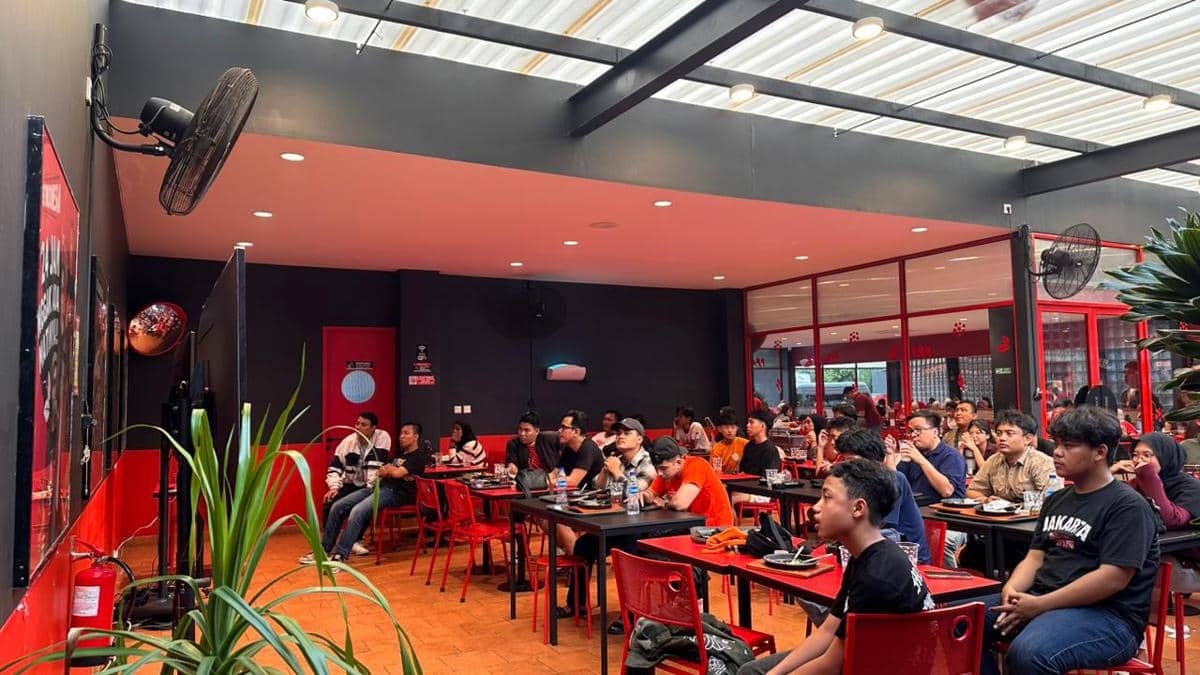 Suasana nobar pertandingan Persija melawan Persib di sebuah kafe dengan pengunjung duduk menyaksikan layar televisi bersama.