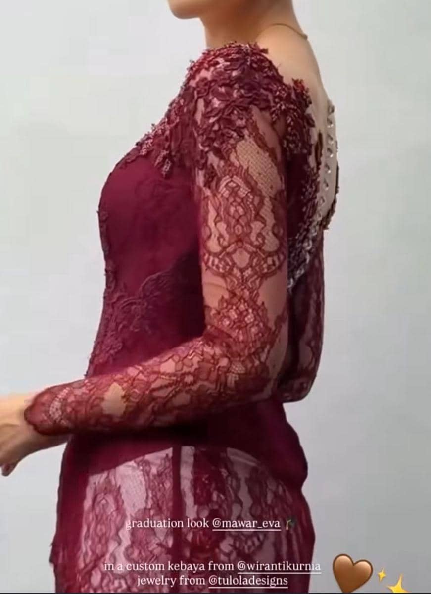 Seorang wanita mengenakan kebaya bordir berwarna marun dengan detail renda transparan di lengan dan punggung saat acara wisuda.
