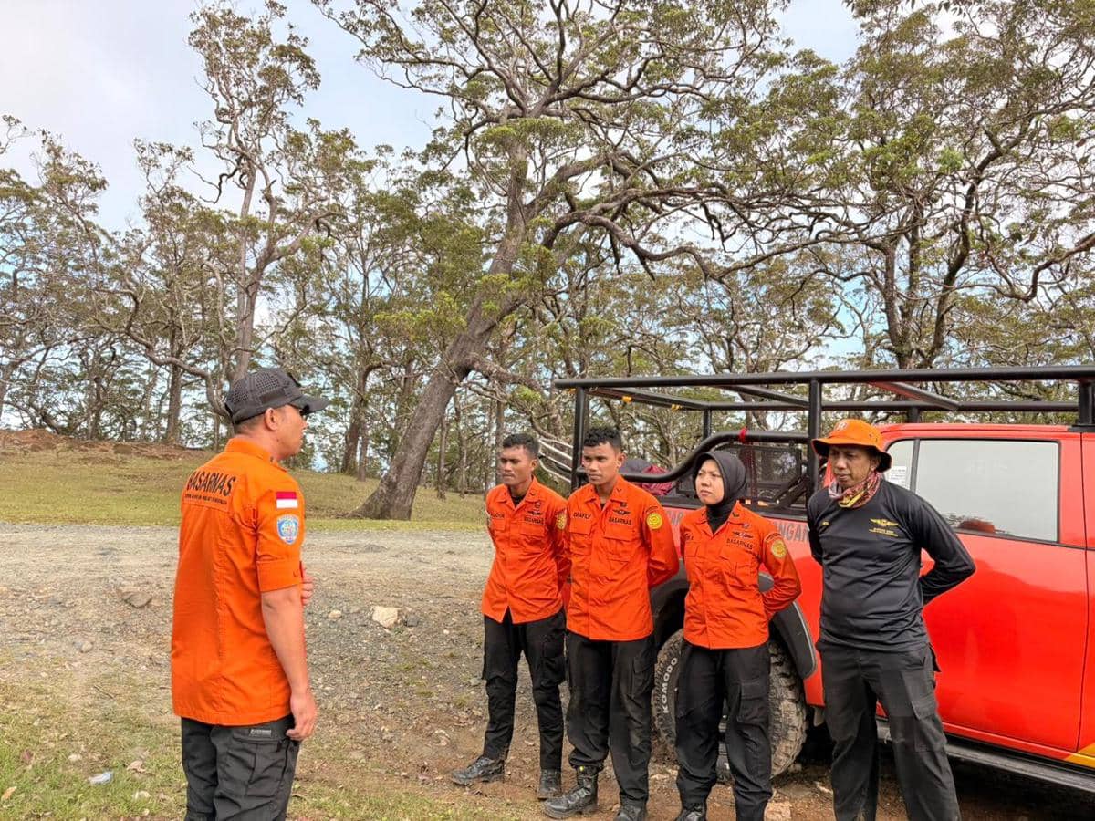 Tim Basarnas Kupang mengenakan seragam oranye berdiri di dekat kendaraan penyelamat di area hutan Mutis saat melakukan briefing pencarian.