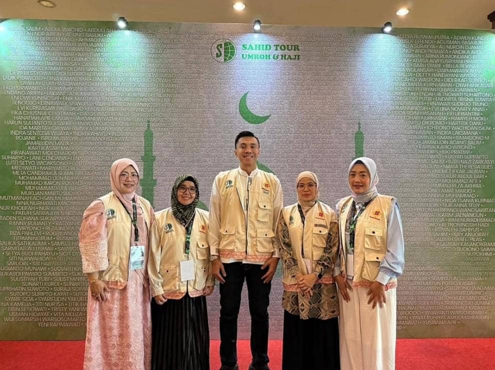 Lima orang calon jamaah haji mengenakan rompi Sahid Tour berfoto bersama di depan latar bertuliskan nama-nama jamaah dan logo bulan sabit hijau.