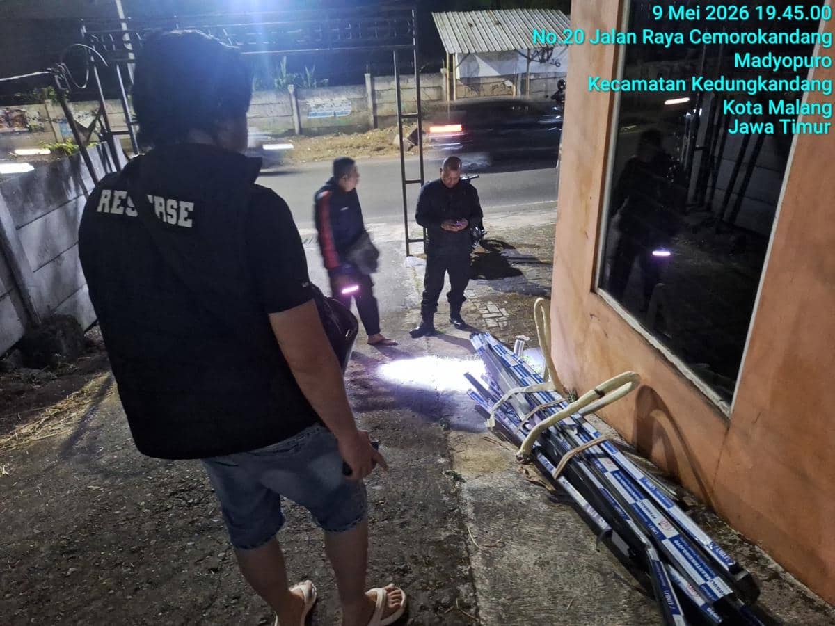 Petugas kepolisian memeriksa area depan kantor pemasaran Perumahan Cemara Diamond Townhouse di Malang pada malam hari.