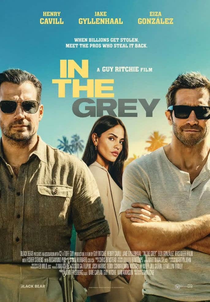 Poster film In the Grey menampilkan tiga karakter utama berdiri dengan latar belakang langit biru dan pohon palem, menciptakan nuansa aksi dan misteri.