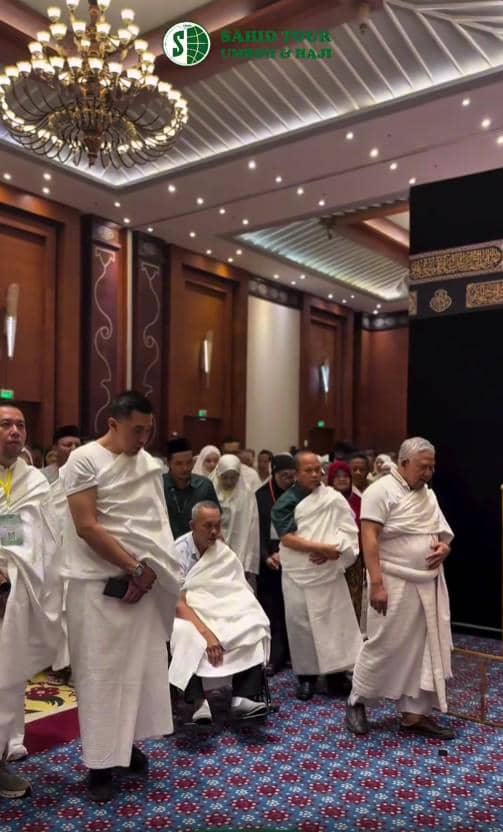 Sejumlah calon jemaah haji mengenakan pakaian ihram putih sedang mengikuti manasik haji di dalam ruangan besar dengan replika Ka'bah.