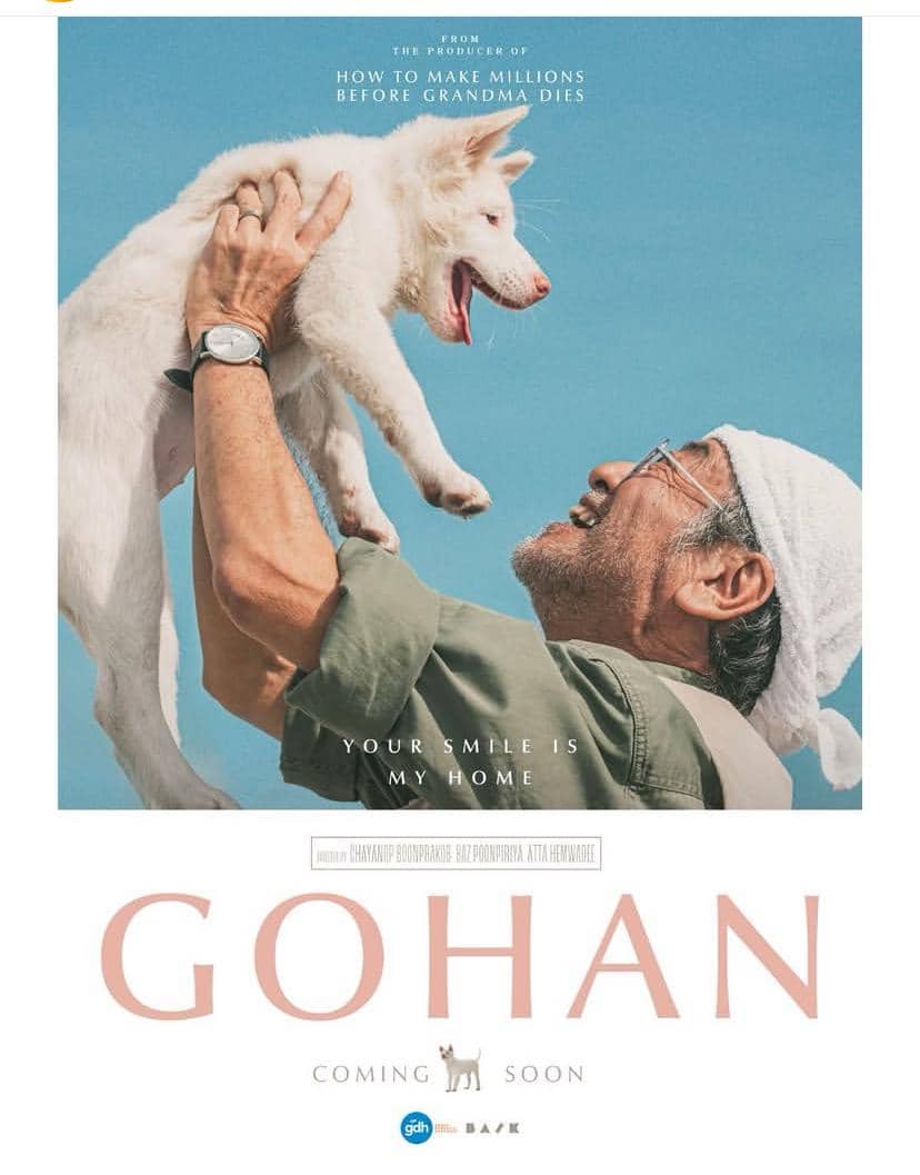 Poster film Gohan menampilkan seorang pria tua tersenyum sambil mengangkat seekor anjing putih di bawah langit biru cerah.