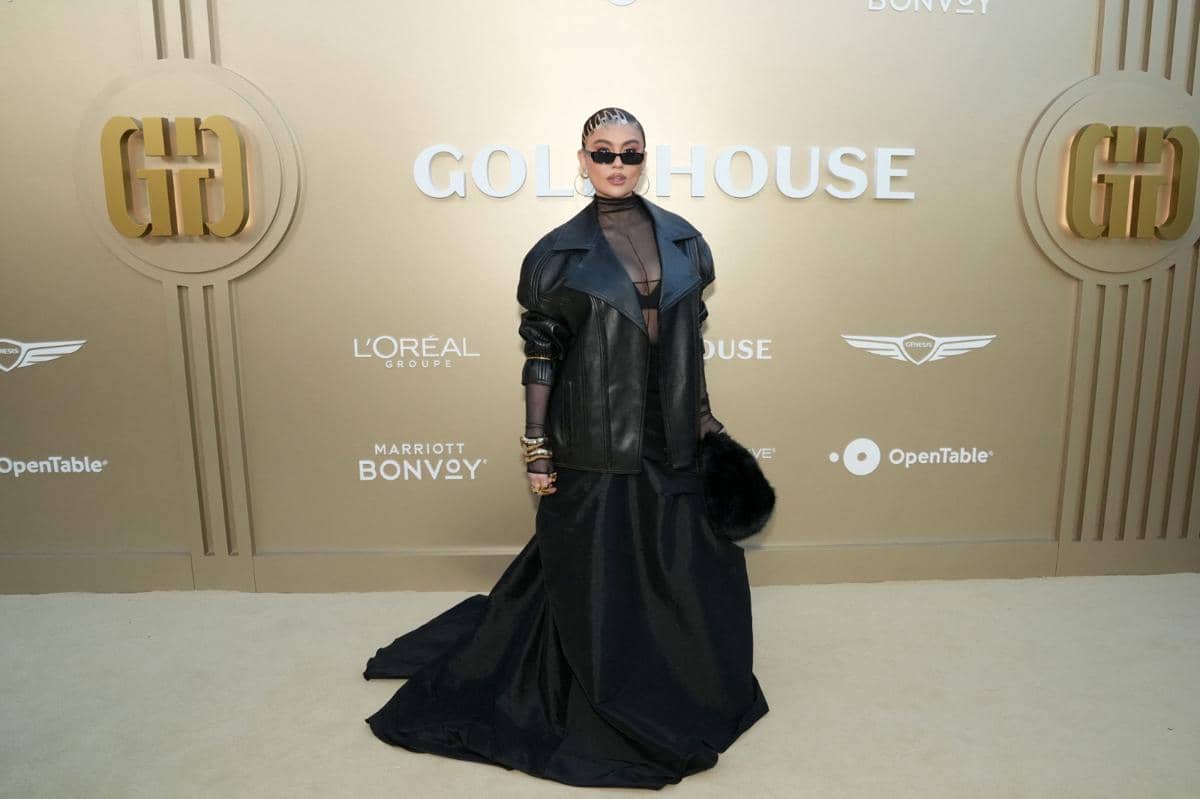 Seorang tamu berpose di karpet emas acara Gold House 5th Annual Gold Gala di The Music Center, Los Angeles, mengenakan gaun hitam elegan dan jaket kulit.