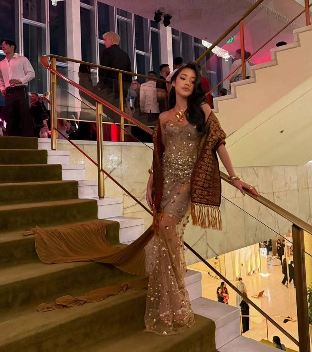 Seorang wanita mengenakan gaun berpayet emas dan selendang tradisional berjalan di tangga mewah saat acara malam di Gold Gala 2026.