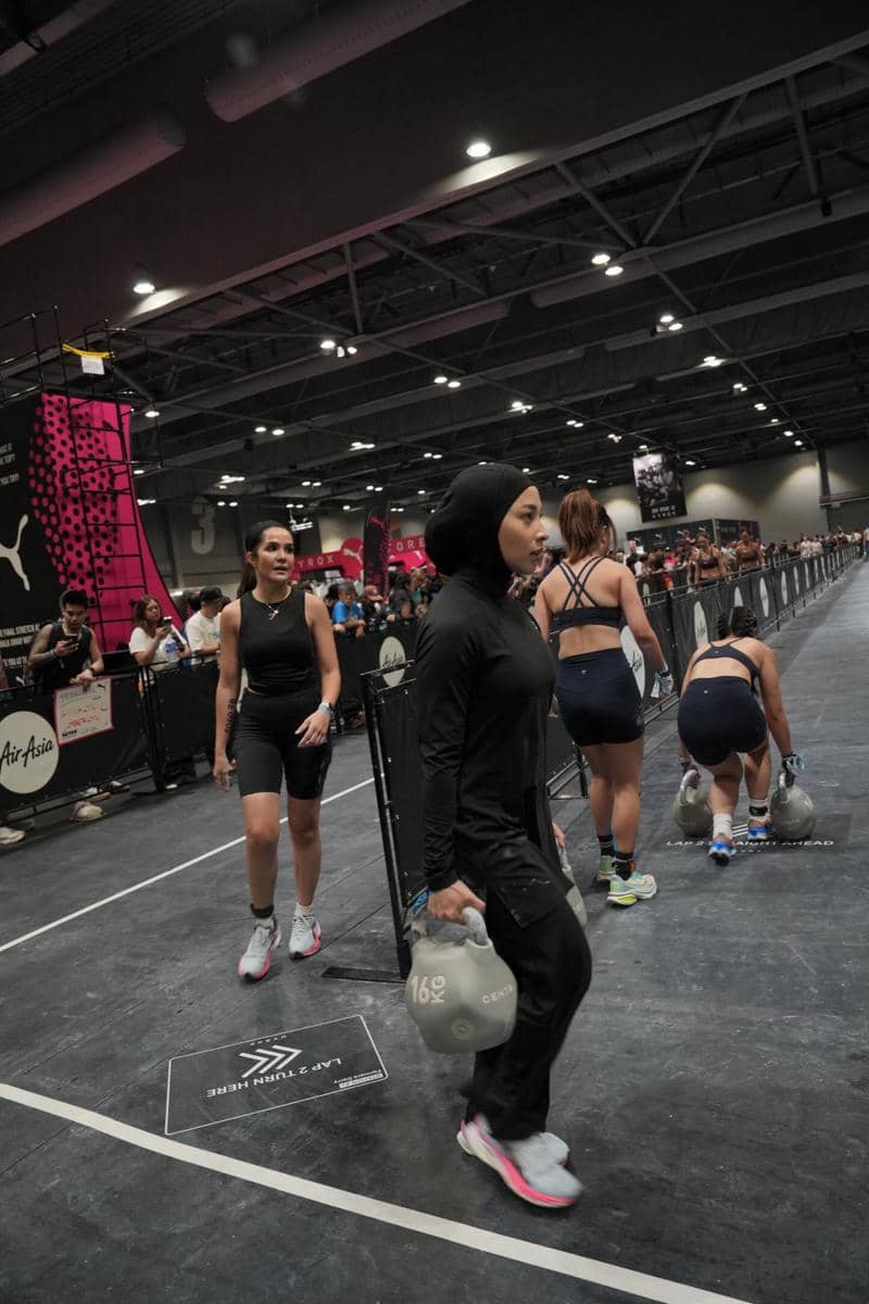 Seorang peserta wanita mengenakan pakaian olahraga hitam membawa beban 16 kg di arena kompetisi Hyrox di Hong Kong.