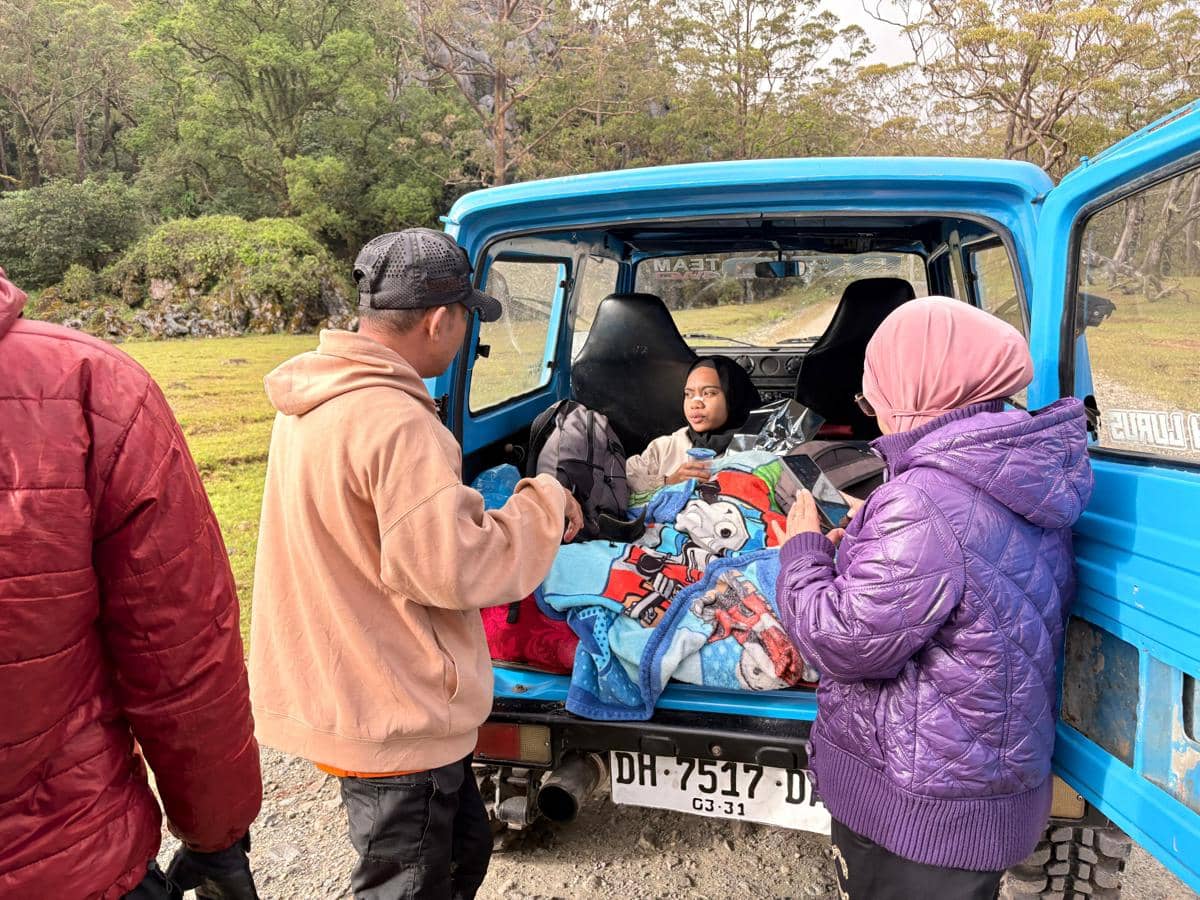 Seorang remaja diselimuti selimut duduk di bagian belakang mobil biru setelah ditemukan, dikelilingi beberapa orang di area pegunungan.