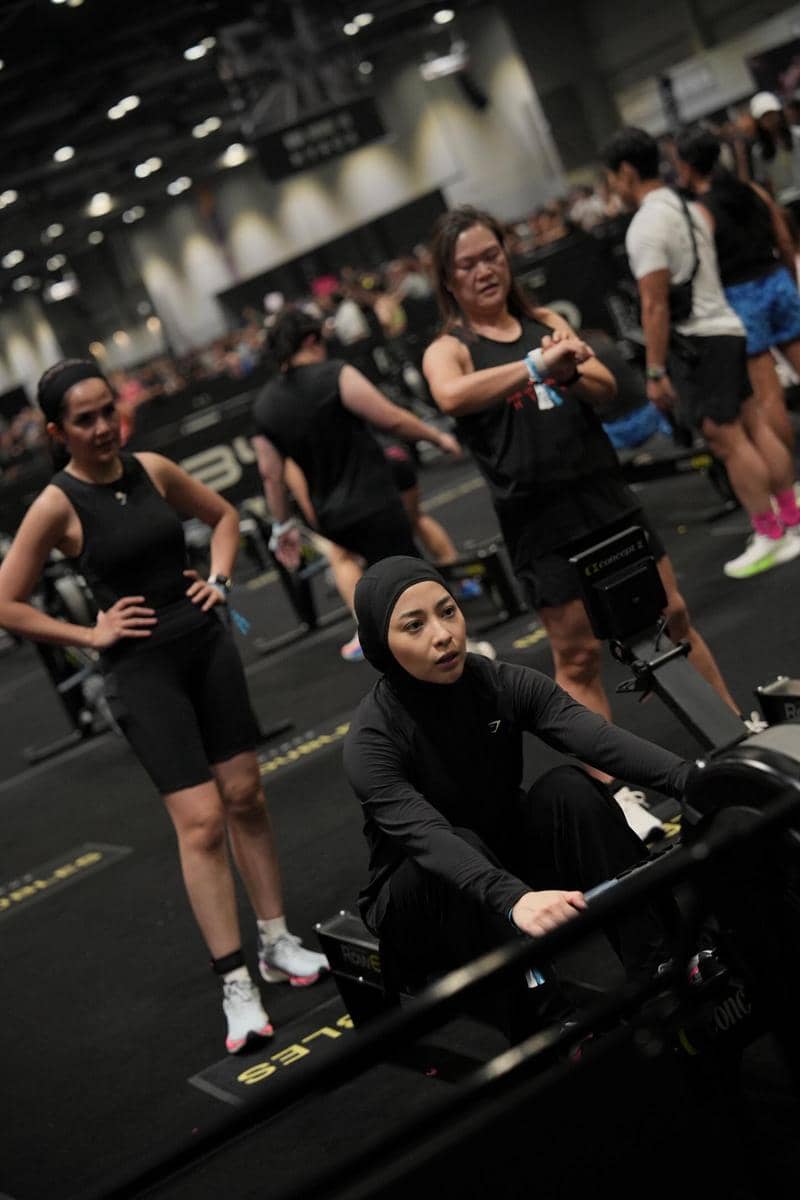 Seorang wanita mengenakan pakaian olahraga hitam sedang menggunakan mesin dayung di arena kompetisi Hyrox di Hong Kong.