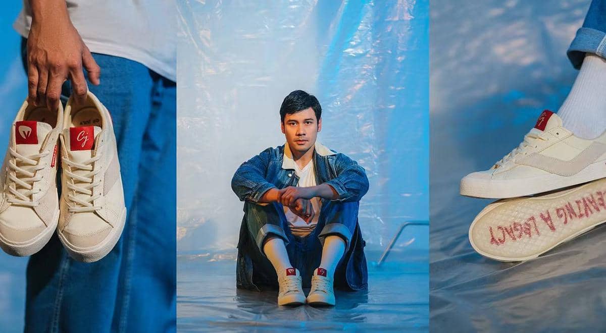 Seorang pria mengenakan jaket denim dan sepatu Ventela berwarna krem dengan detail merah, duduk di lantai dengan latar biru.
