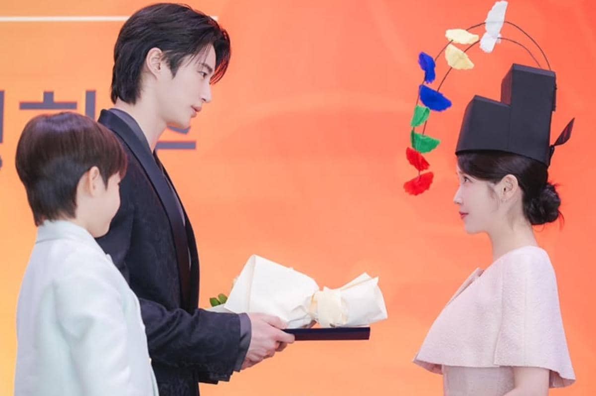 Adegan dari drama Korea Perfect Crown memperlihatkan dua karakter saling berhadapan, satu mengenakan topi unik dengan hiasan warna-warni.