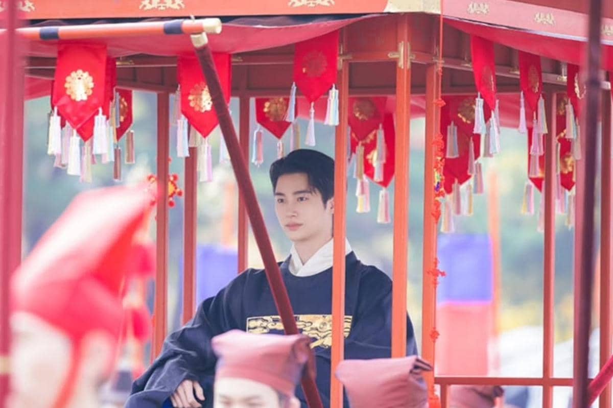 Seorang aktor mengenakan hanbok kerajaan duduk di dalam tandu berhias merah dalam adegan drama Korea Perfect Crown.