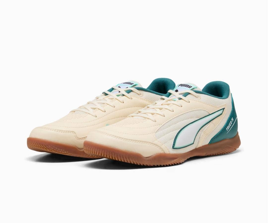 Sepasang sepatu futsal Puma TRUCO IV berwarna krem dengan aksen hijau toska dan sol karet cokelat, tampak dari sisi depan.