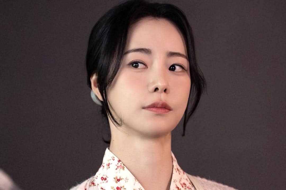 Seorang wanita berambut hitam dengan ekspresi serius mengenakan pakaian bermotif bunga dalam cuplikan drama My Royal Nemesis.