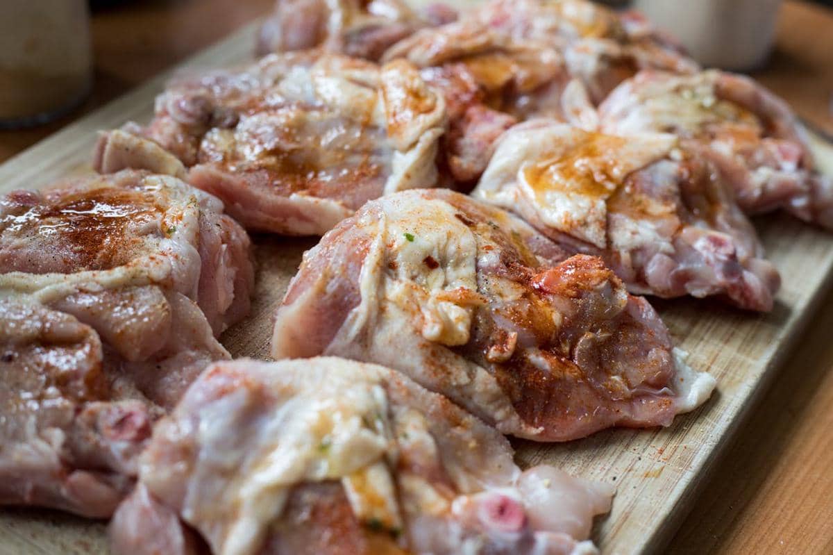 Beberapa potongan paha ayam mentah dibumbui rempah dan minyak di atas talenan kayu siap dimasak ala Provence.