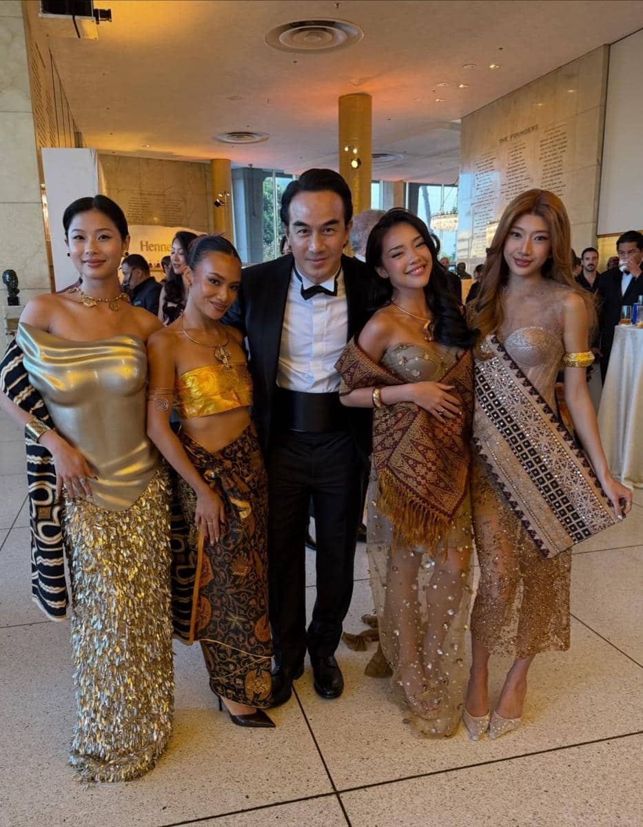 Lima orang berpose bersama di acara gala dengan busana formal dan tradisional bernuansa emas dan cokelat di ruang elegan.