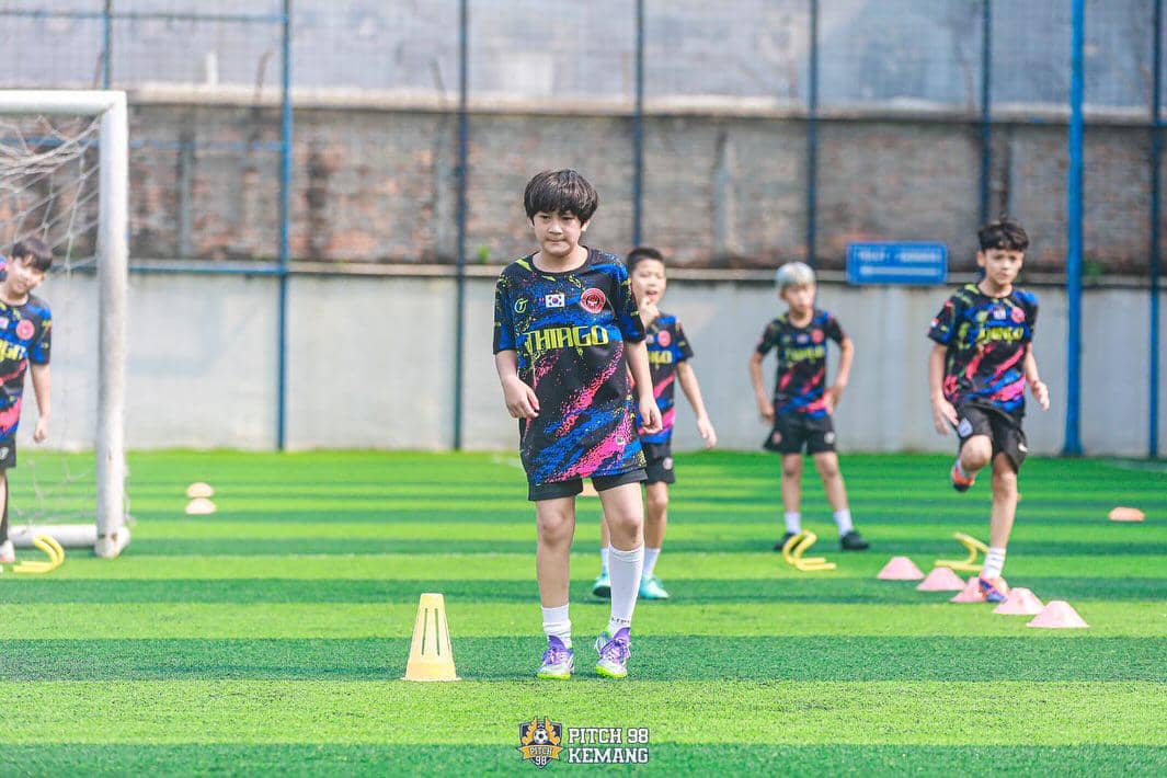 Beberapa anak mengenakan seragam sepak bola berlatih di lapangan hijau dengan cone latihan di Pitch 98 Kemang.