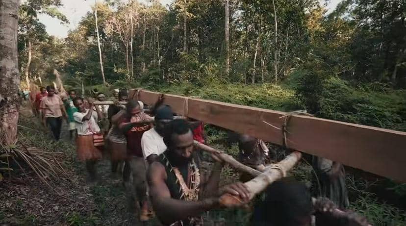 Sekelompok orang berjalan di hutan sambil memikul balok kayu besar dalam adegan film Pesta Babi.