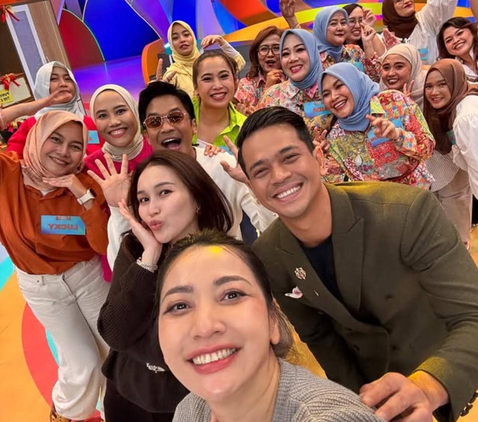 Sekelompok orang tersenyum dan berpose ceria bersama di studio berwarna cerah saat mengikuti acara kuis arisan.