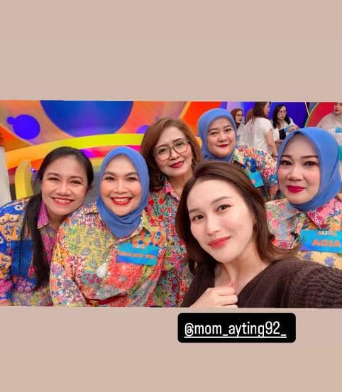 Sekelompok wanita tersenyum berpose bersama di studio berwarna cerah, mengenakan busana bermotif cerah dan kerudung biru muda.