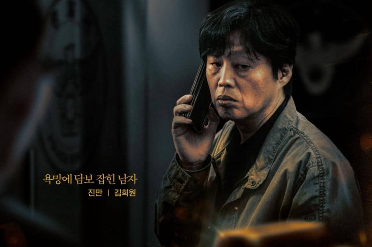Seorang pria berjaket abu-abu memegang ponsel di telinganya dengan ekspresi serius dalam adegan drama Gold Land.