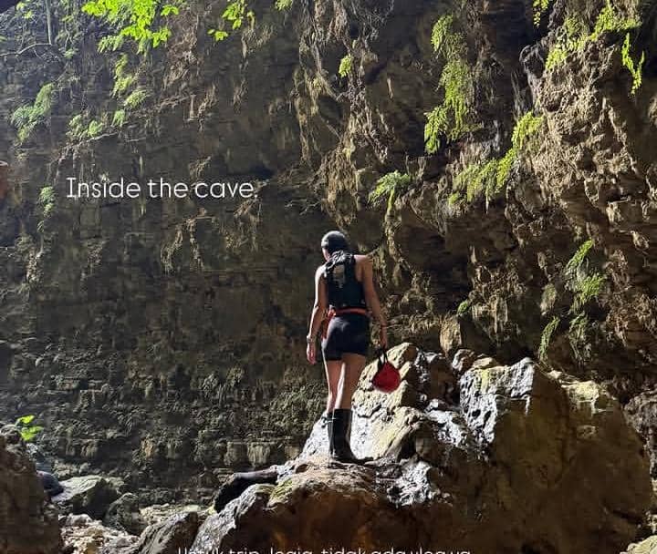 Seorang perempuan berdiri di dalam Gua Ngeleng dengan perlengkapan pendakian, dikelilingi dinding batu dan lumut hijau.