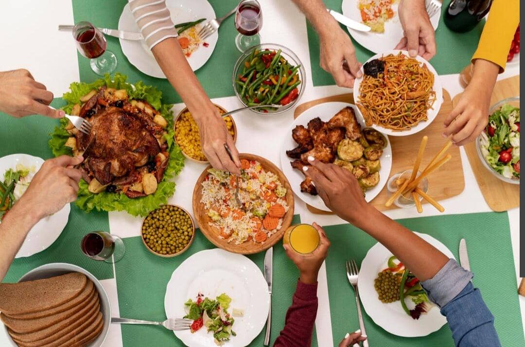 Ilustrasi orang menikmati makan bersama sambil duduk di meja makan dengan berbagai hidangan di hadapan mereka.