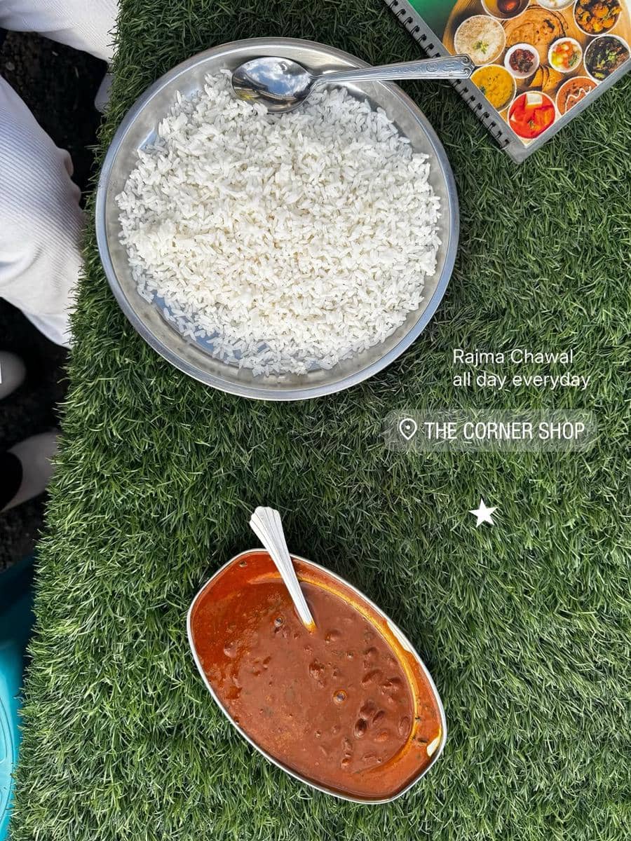 Semangkuk nasi putih dan semangkuk kari kacang merah disajikan di atas meja berlapis rumput sintetis dengan sendok di masing-masing mangkuk.