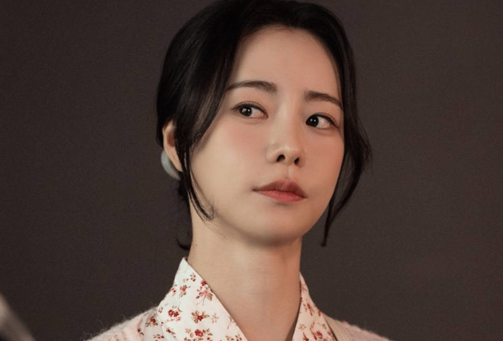 Seorang wanita berambut hitam dengan ekspresi serius mengenakan pakaian bermotif bunga dalam cuplikan drama Korea My Royal Nemesis.