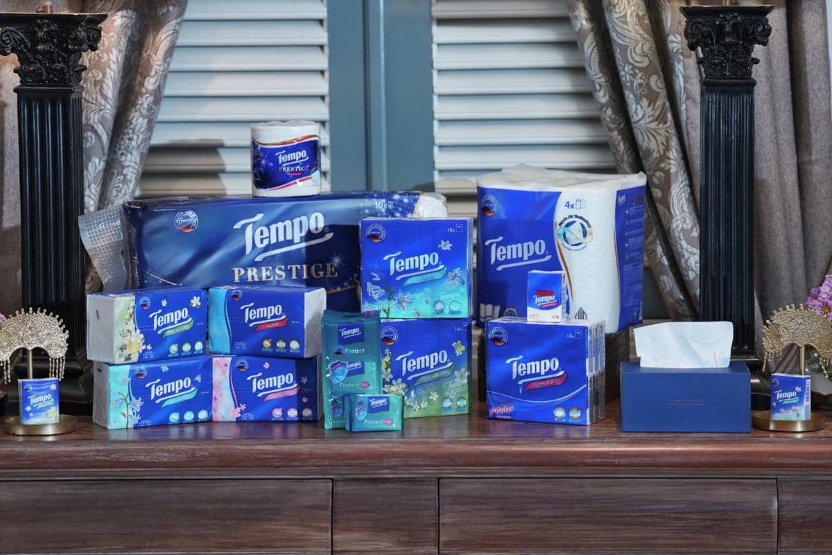 Beragam produk tisu merek Tempo, termasuk Tempo Prestige dan varian lainnya, tersusun rapi di atas meja kayu dengan latar tirai elegan.