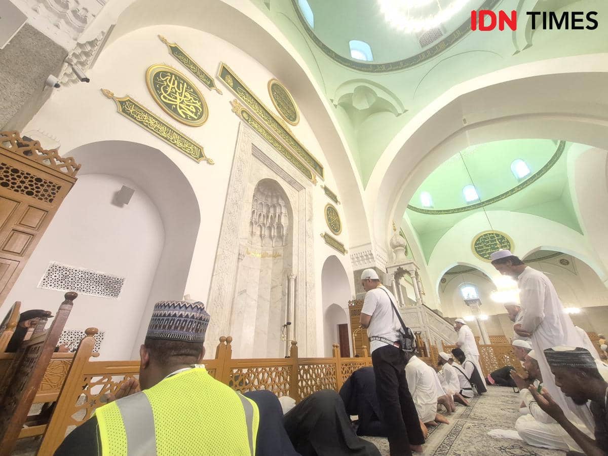 Jemaah sedang berdoa di dalam Masjid Quba dengan latar mihrab dan mimbar berarsitektur indah serta kaligrafi Arab di dinding.