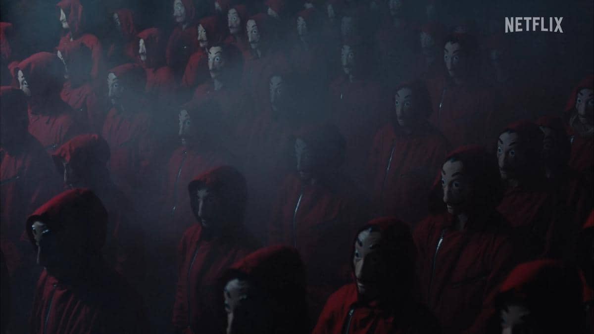 Sekelompok orang mengenakan jumpsuit merah dan topeng ikonik berdiri dalam kabut tebal, menampilkan suasana misterius dari teaser Money Heist.