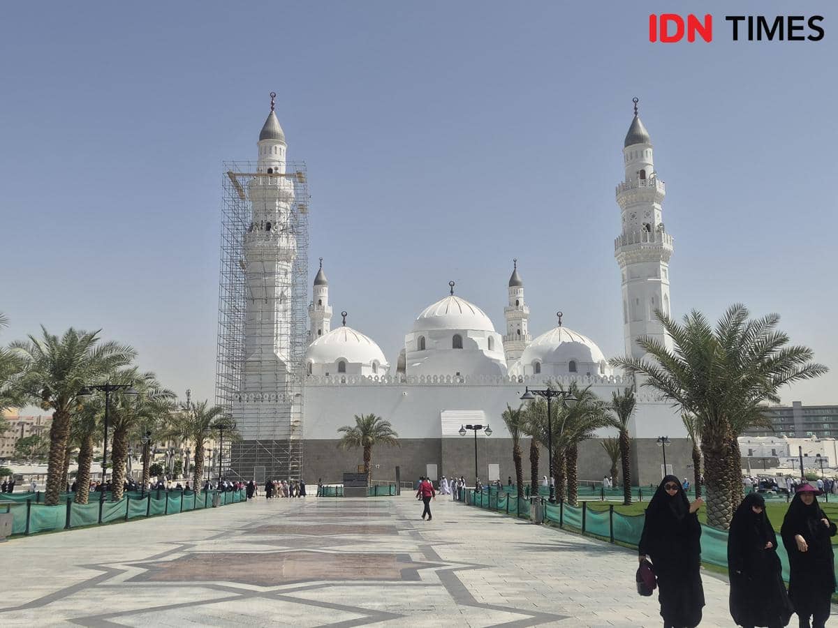 Masjid Quba dengan kubah putih dan menara tinggi di bawah langit cerah, dikelilingi pohon palem serta pejalan kaki di area halaman.
