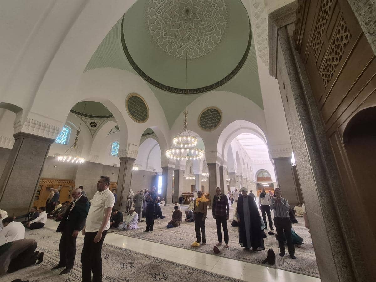 Bagian dalam Masjid Quba dengan jamaah yang sedang berdiri dan duduk di area shalat, menampilkan kubah dan lampu gantung megah.