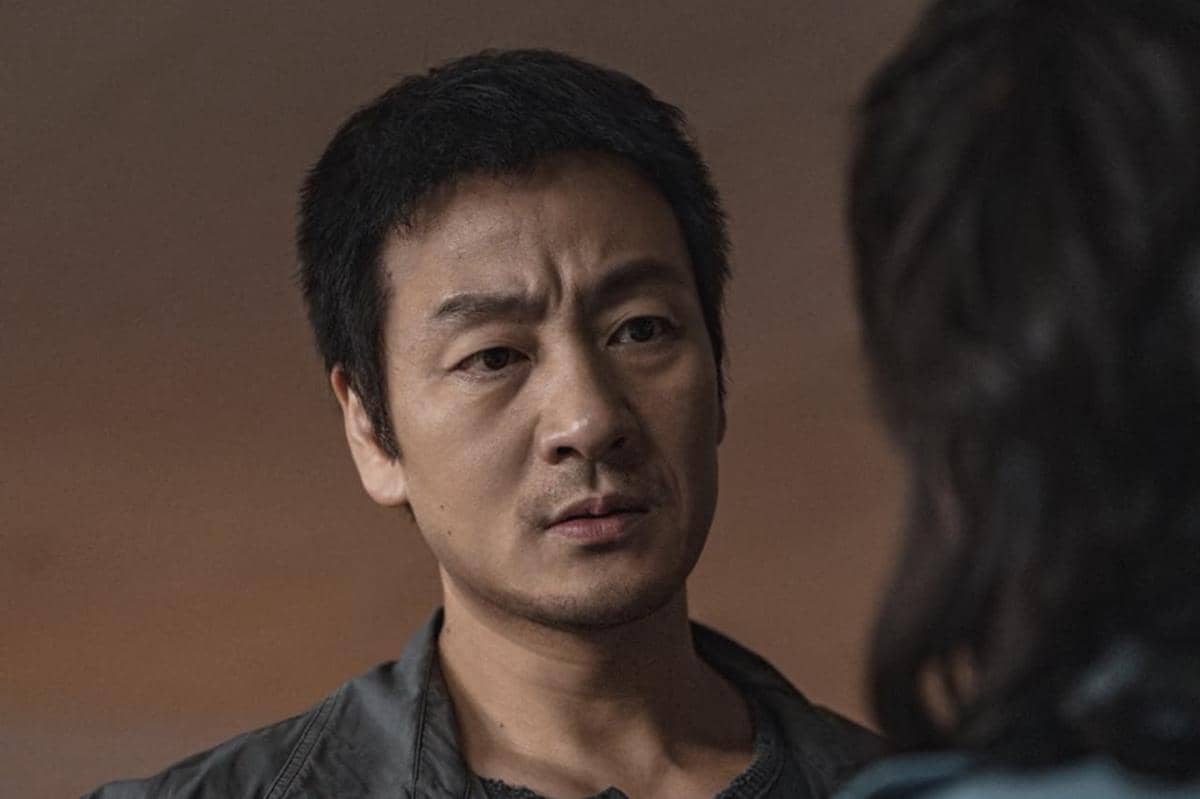 Seorang pria berwajah serius mengenakan jaket gelap sedang menatap seseorang di depannya dalam adegan drama The Scarecrow.