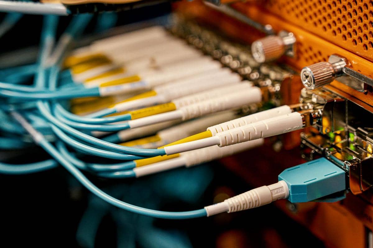 Beberapa kabel optik berwarna biru dan putih terhubung ke panel jaringan dengan konektor logam di ruang server.