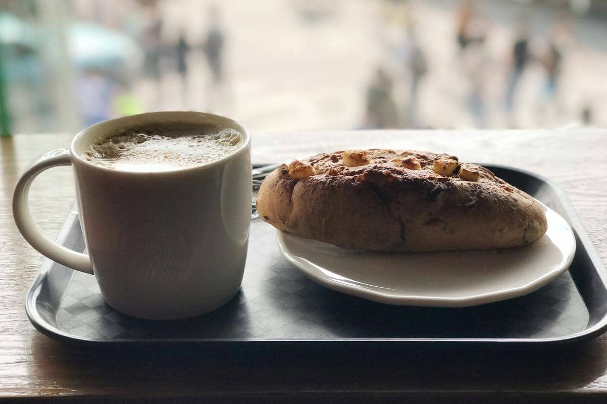 Roti salt bread dengan olesan garlic butter disajikan di atas piring putih bersama secangkir kopi panas di atas nampan hitam.