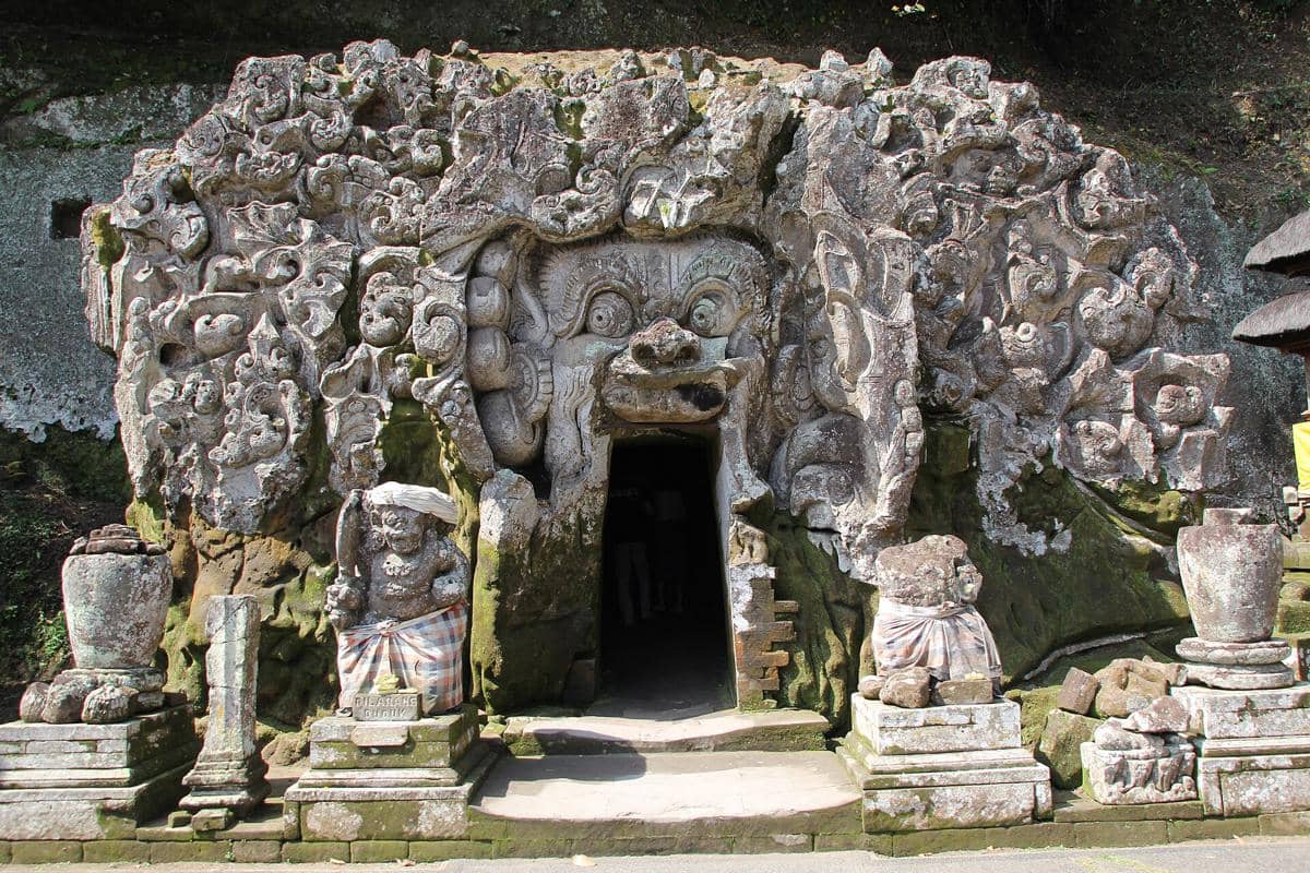 Pintu masuk Goa Gajah di Bali dengan ukiran batu kuno berbentuk wajah raksasa dan patung penjaga di kedua sisinya.