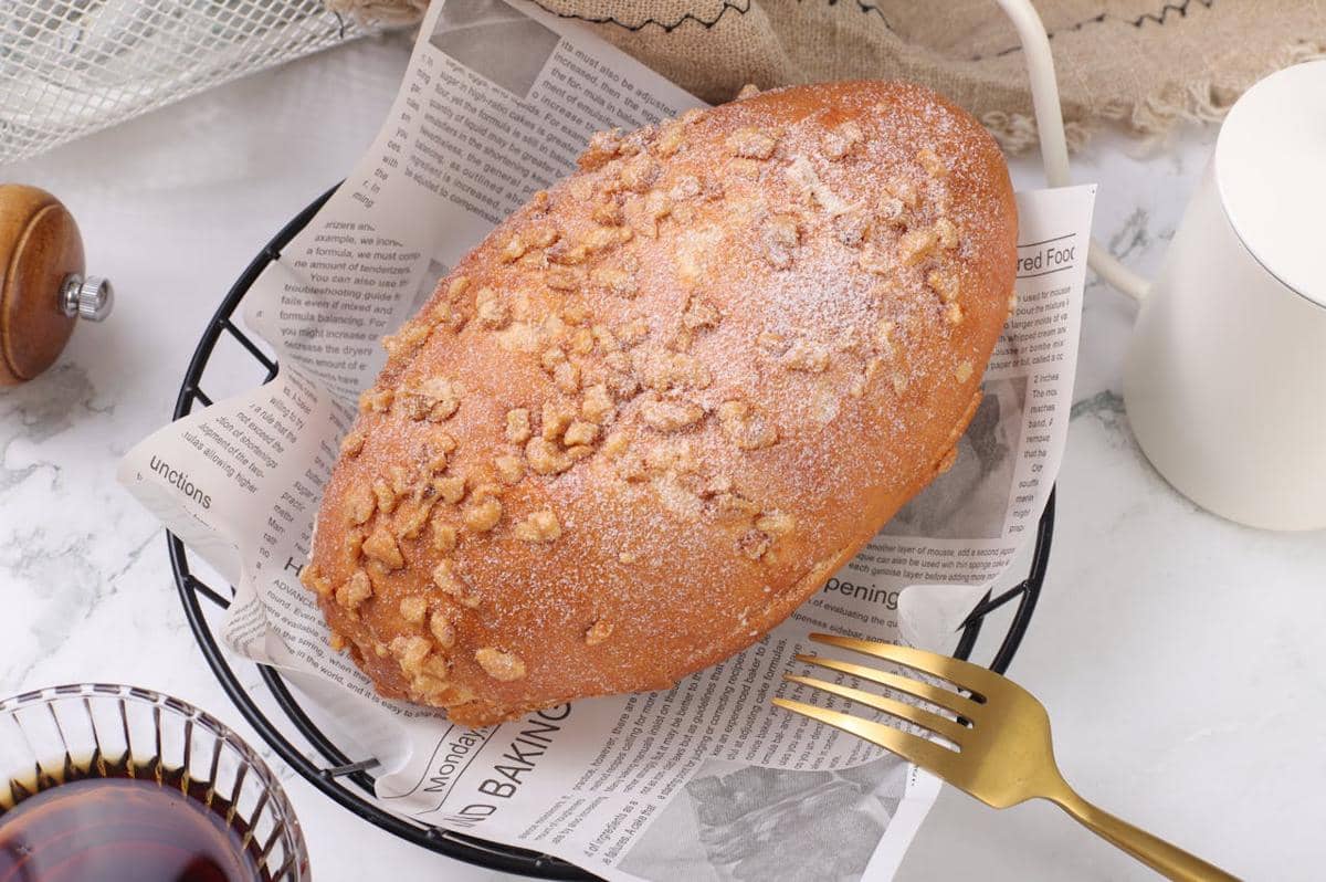 Roti salt bread dengan topping coffee bun berwarna keemasan disajikan di atas kertas koran dalam keranjang hitam di meja marmer.