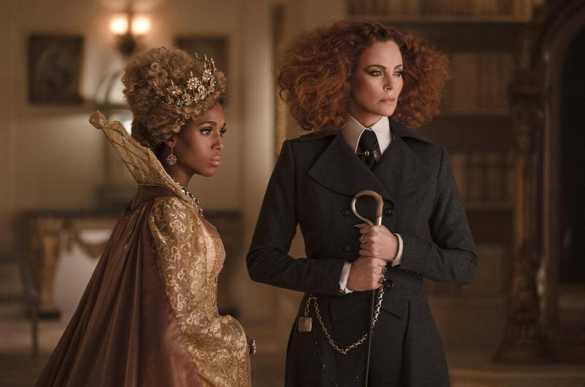 Dua karakter dalam film The School for Good and Evil berdiri berdampingan, satu mengenakan gaun emas berhias mahkota dan satu berjas gelap memegang tongkat.