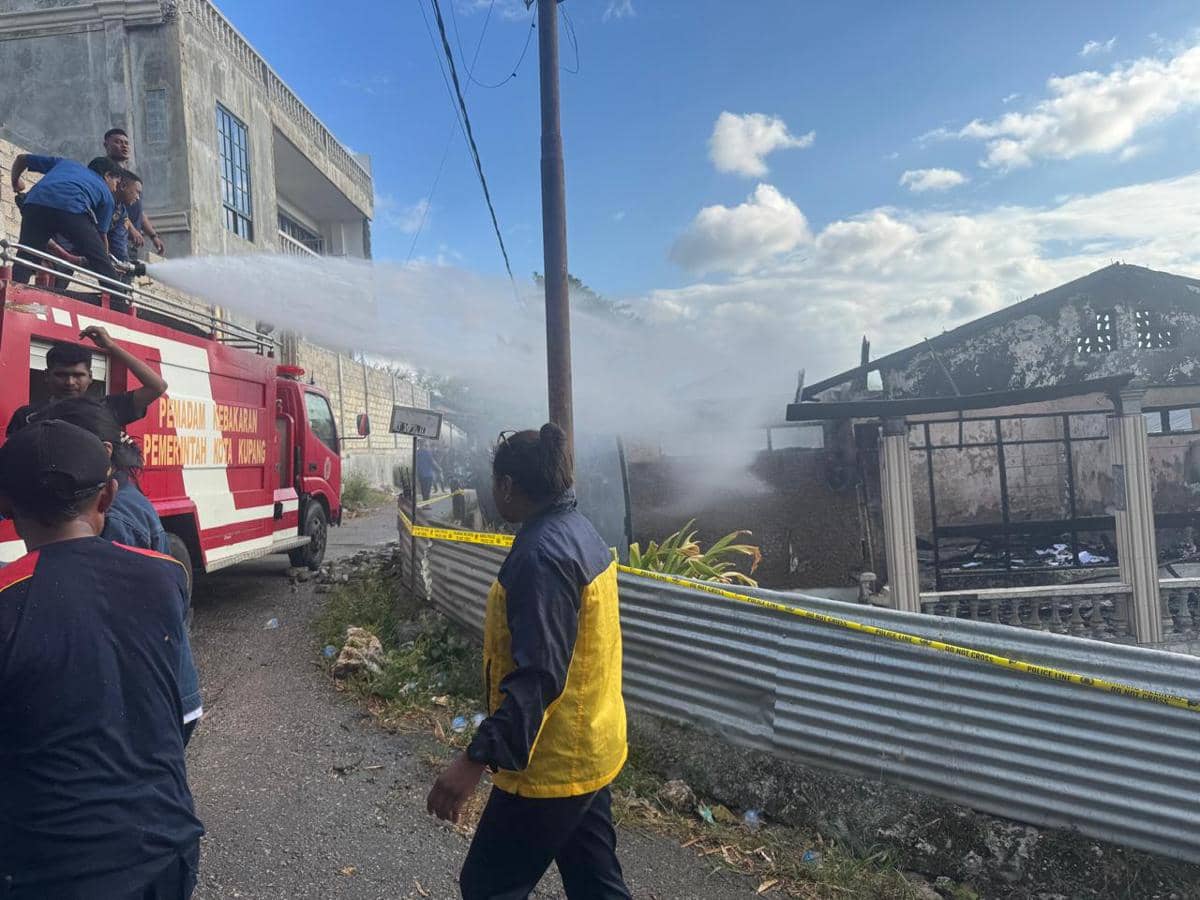 Petugas pemadam kebakaran Kupang menyemprot air ke arah bangunan panti asuhan yang hangus terbakar di bawah langit cerah.