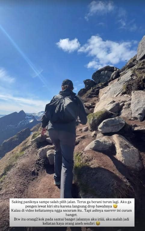 Seorang pria berjalan mendaki jalur berbatu di pegunungan Norwegia dengan langit biru cerah dan pemandangan lembah di kejauhan.
