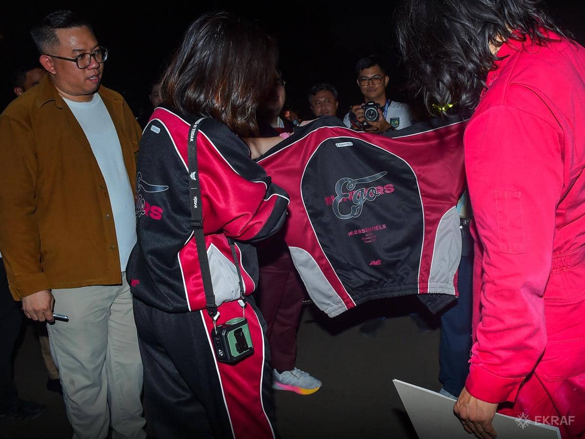 Beberapa orang berinteraksi di acara The Elite Showcase 2026, salah satunya memegang jaket berwarna hitam dan merah marun.